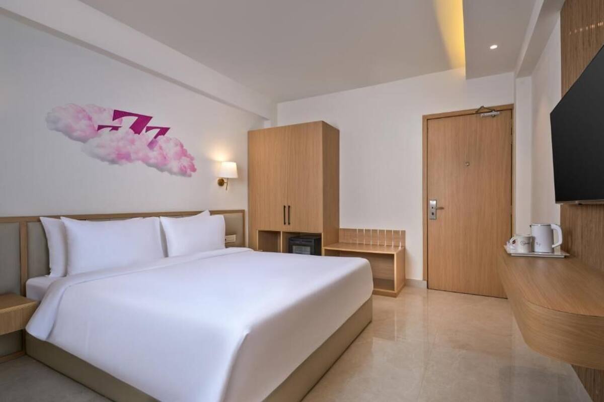 Quarto de hotel com uma cama, um guarda-roupa de madeira, uma televisão e um candeeiro fixo na parede.