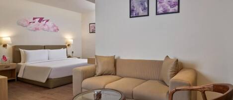 Una habitación de hotel con una cama, un sofá, una mesa de centro de vidrio y dos cuadros en la pared.