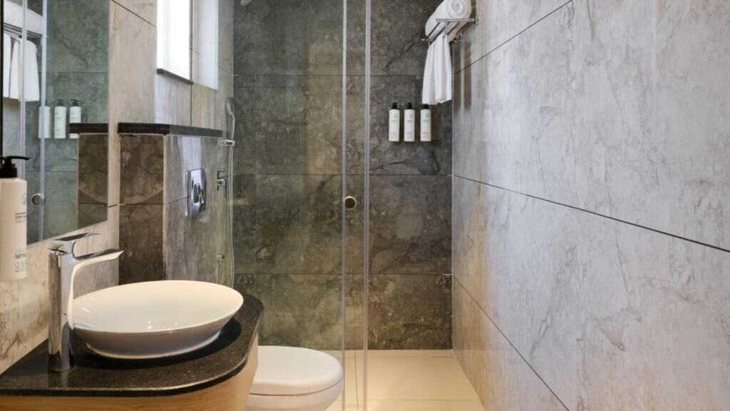 A modern bathroom with a glass-enclosed shower, a sink with a marble countertop, and a toilet.