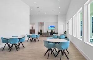 Ein moderner Konferenzraum mit runden Tischen und blauen Stühlen, großen Fenstern und einem Fernsehbildschirm.
