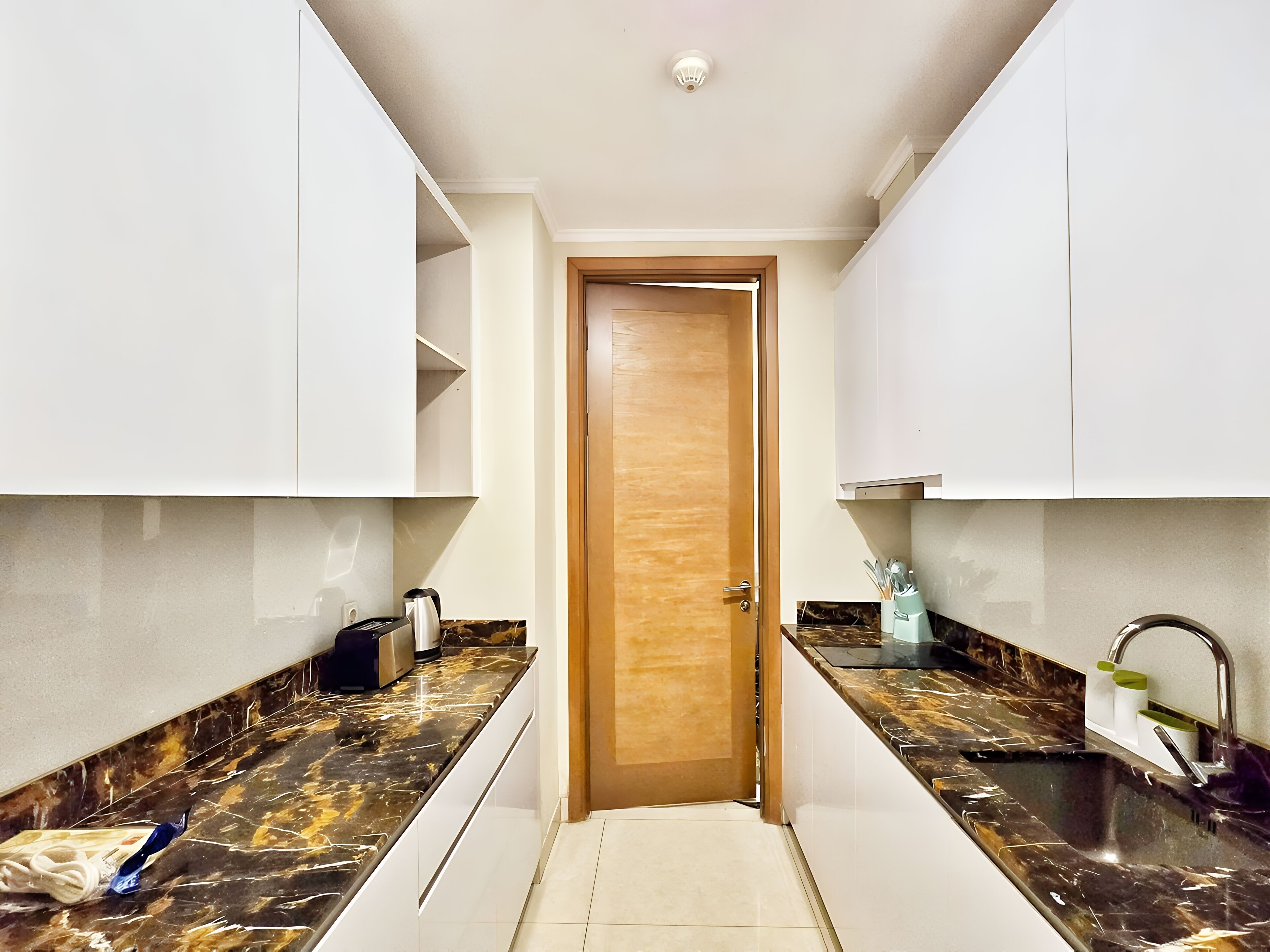 A narrow kitchen with white cabinets, a wooden door, and black marble countertops.