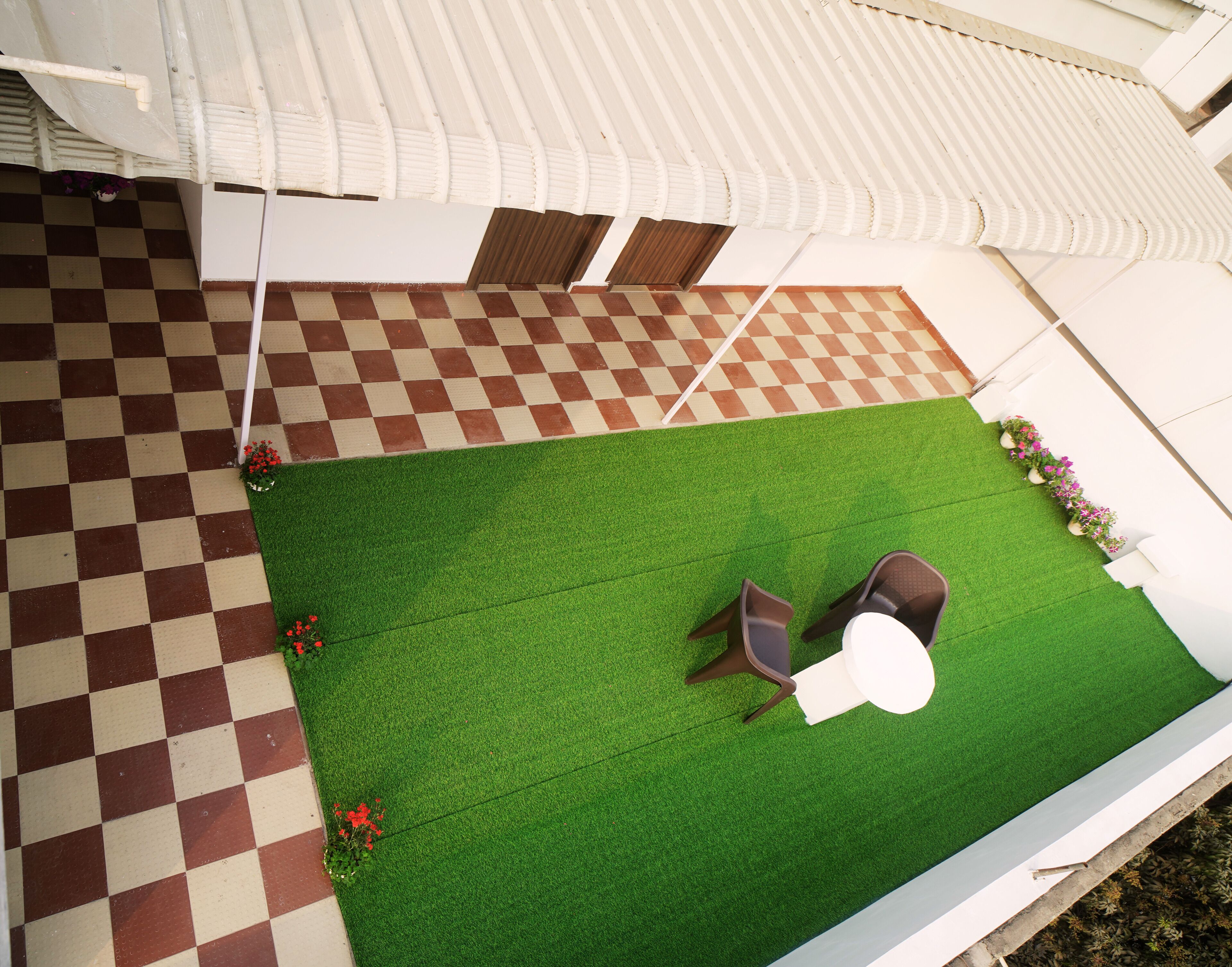A rooftop terrace with a checkered floor, green artificial grass, and two chairs.