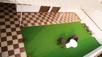 A rooftop terrace with a checkered floor, green artificial grass, and two chairs.