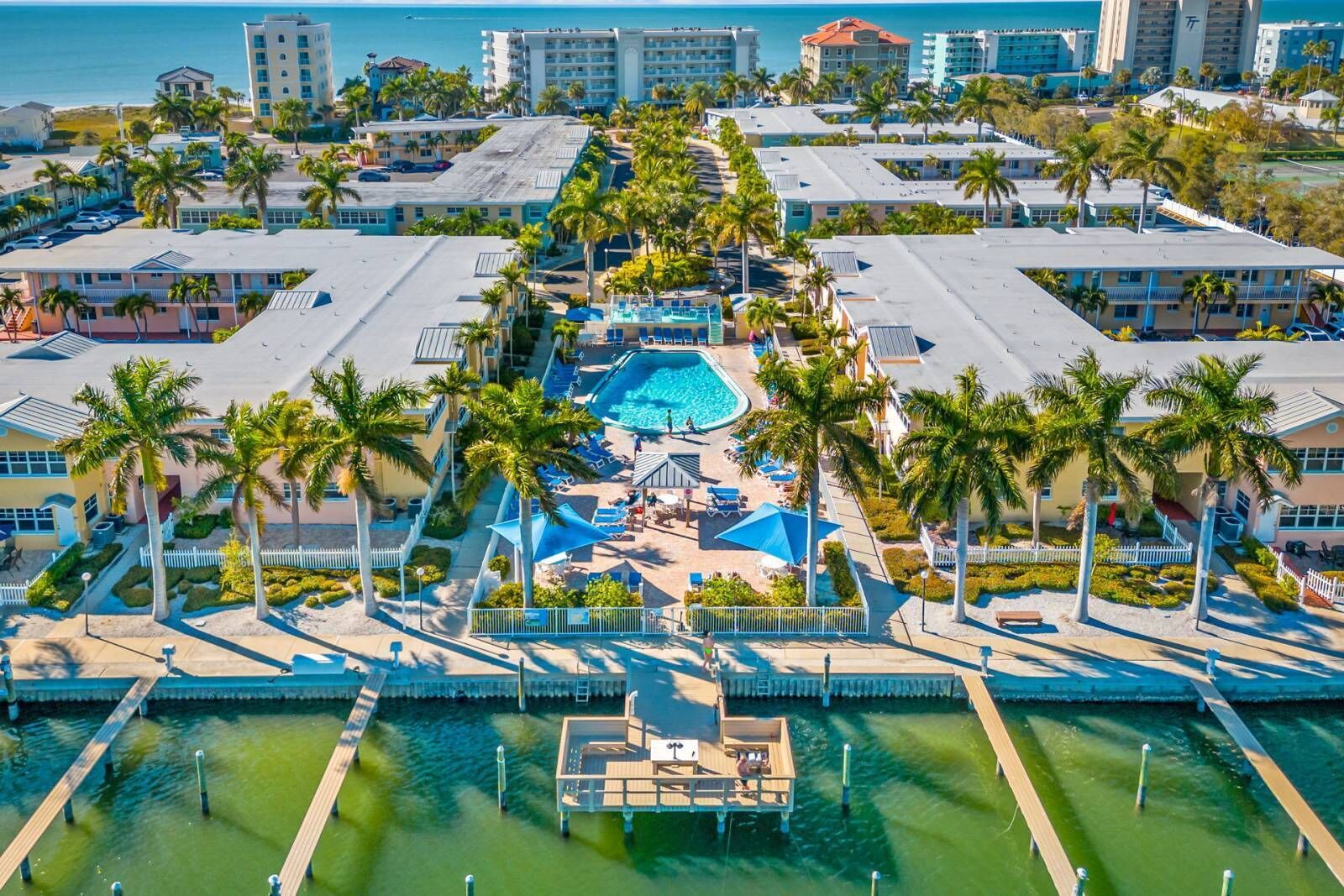 Eine Vogelperspektive zeigt ein Resort mit einem zentralen Schwimmbecken, mehreren Gästegebäuden und Palmen.