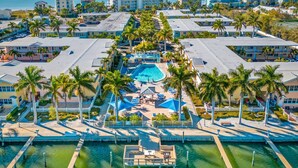 Eine Vogelperspektive zeigt ein Resort mit einem zentralen Schwimmbecken, mehreren Gästegebäuden und Palmen.