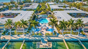 Eine Vogelperspektive zeigt ein Resort mit einem zentralen Schwimmbecken, mehreren Gästegebäuden und Palmen.