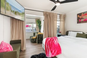 Une chambre d’hôtel avec un lit, une chaise, un bureau, un ventilateur de plafond et une grande fenêtre.