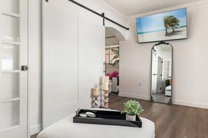 Une chambre d’hôtel dotée d’une porte coulissante, d’un téléviseur à écran plat, d’un miroir, d’un plateau avec des bougies et d’une petite plante.