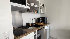 Uma cozinha compacta com armários brancos, bancada preta, lava-louças embutida e uma pequena lixeira.