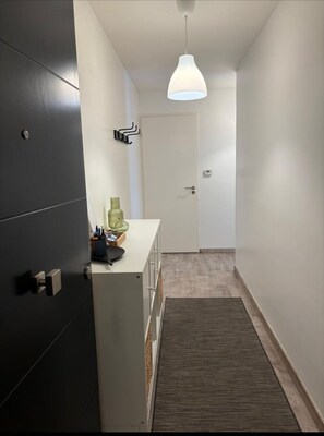 A hallway with a modern light fixture, a door, and a counter with items on it. - 2-room apartment ideally located: walk to the train station/Villepinte/CDG/Paris exhibition center (Aulnay-sous-Bois)