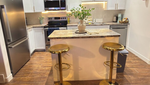 A modern kitchen with white cabinets, stainless steel appliances, a granite countertop, and two gold stools.