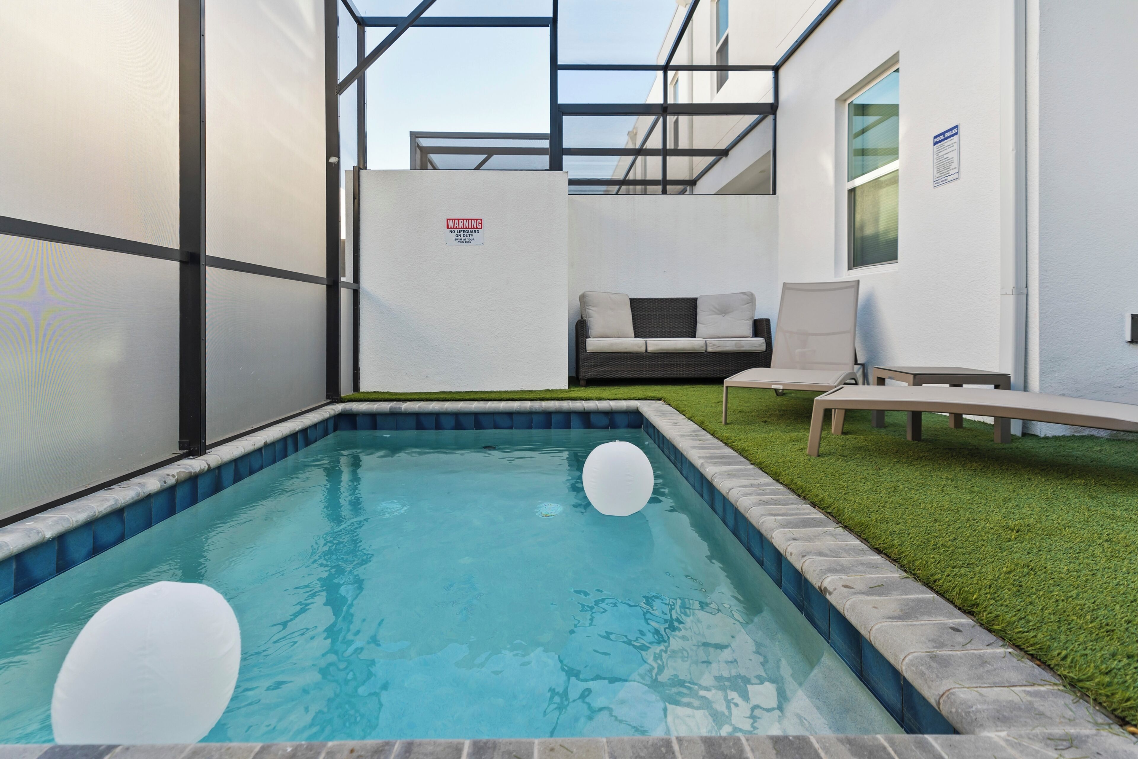En swimmingpool med et glasafskærmning, et loungeområde med sofa og stole, og et skilt med teksten 'No Swimming'.