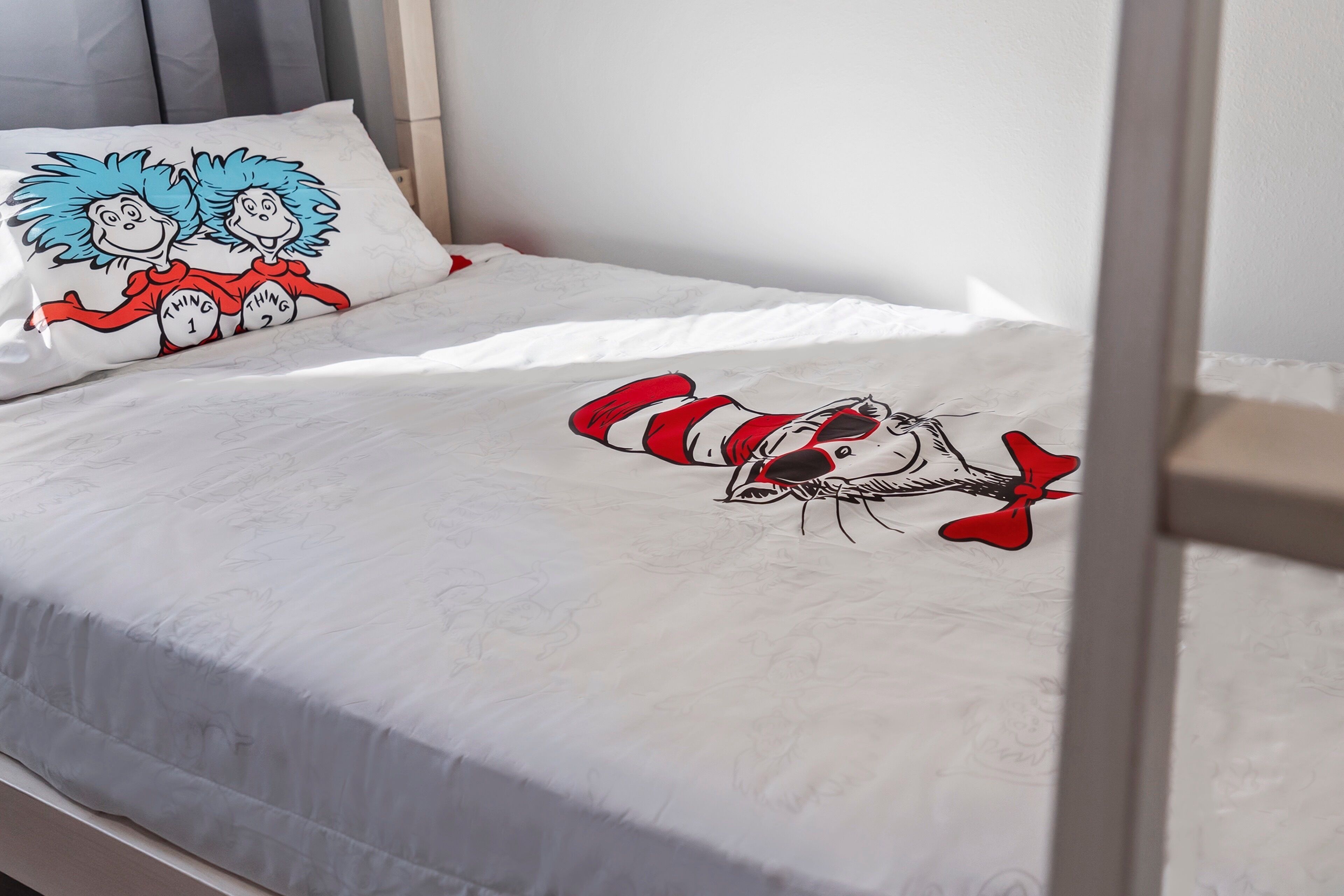 Una cama con sábana blanca decorada con un diseño de personaje, un almohadón con un diseño de personaje y un cabecero.
