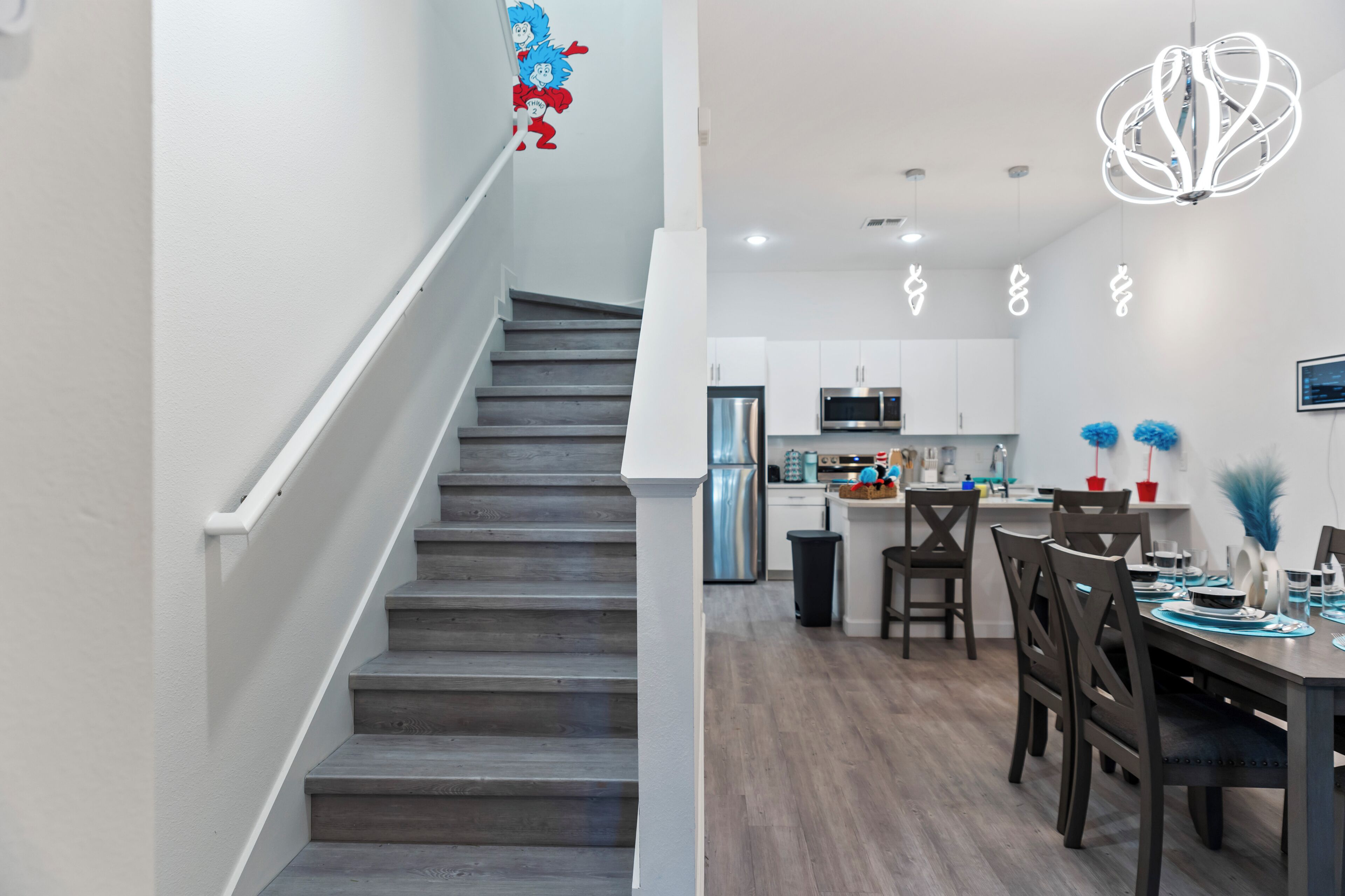 A modern kitchen with stainless steel appliances, a dining area with dark wooden furniture, and a staircase with white railings.