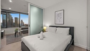 Een moderne hotelkamer met een groot bed, uitzicht over de stad, een klein bureau en een lijst met kunstwerk aan de muur.
