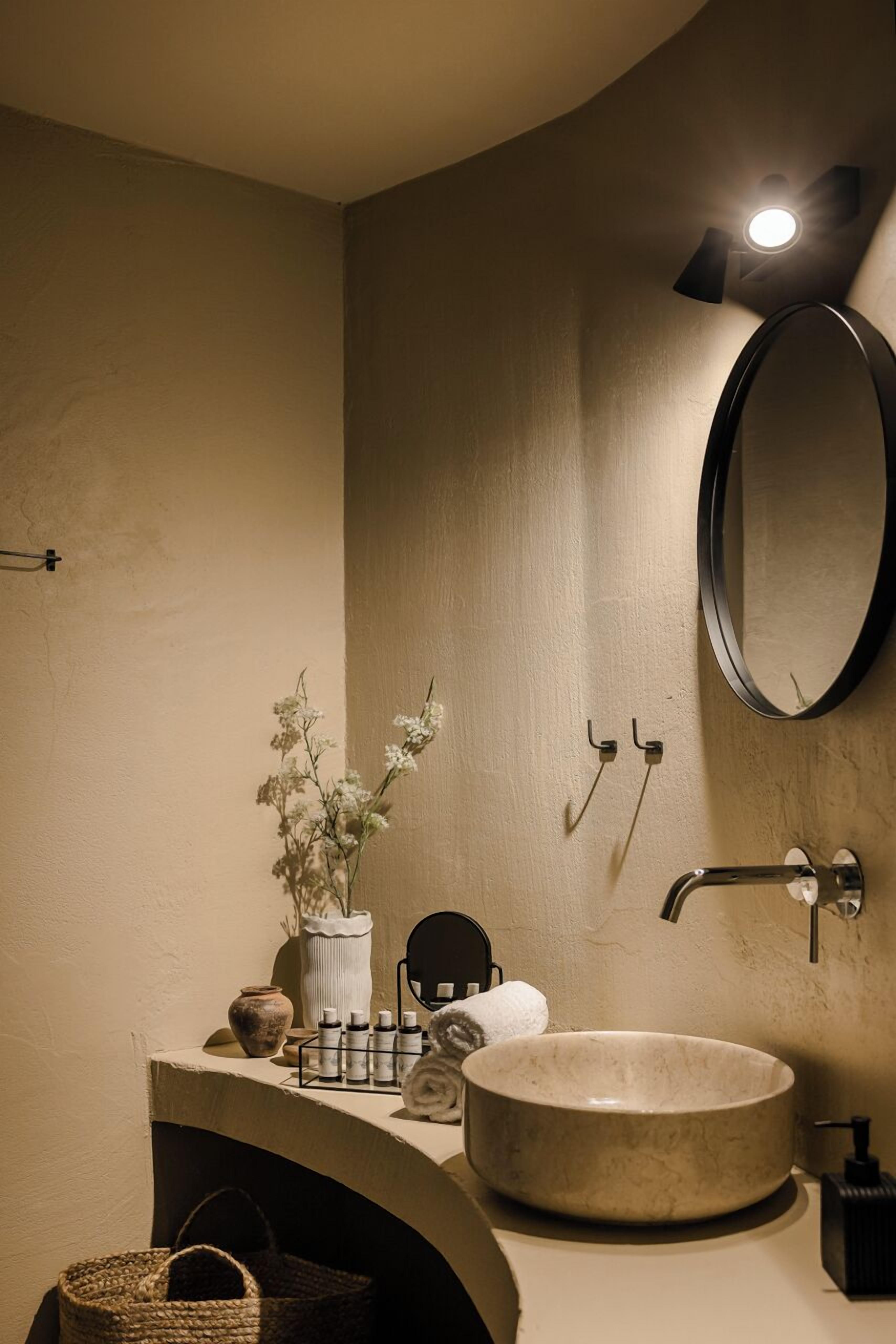 Een badkamer met een rond wastafel, een spiegel, een handdoekhouder en een kleine plant.