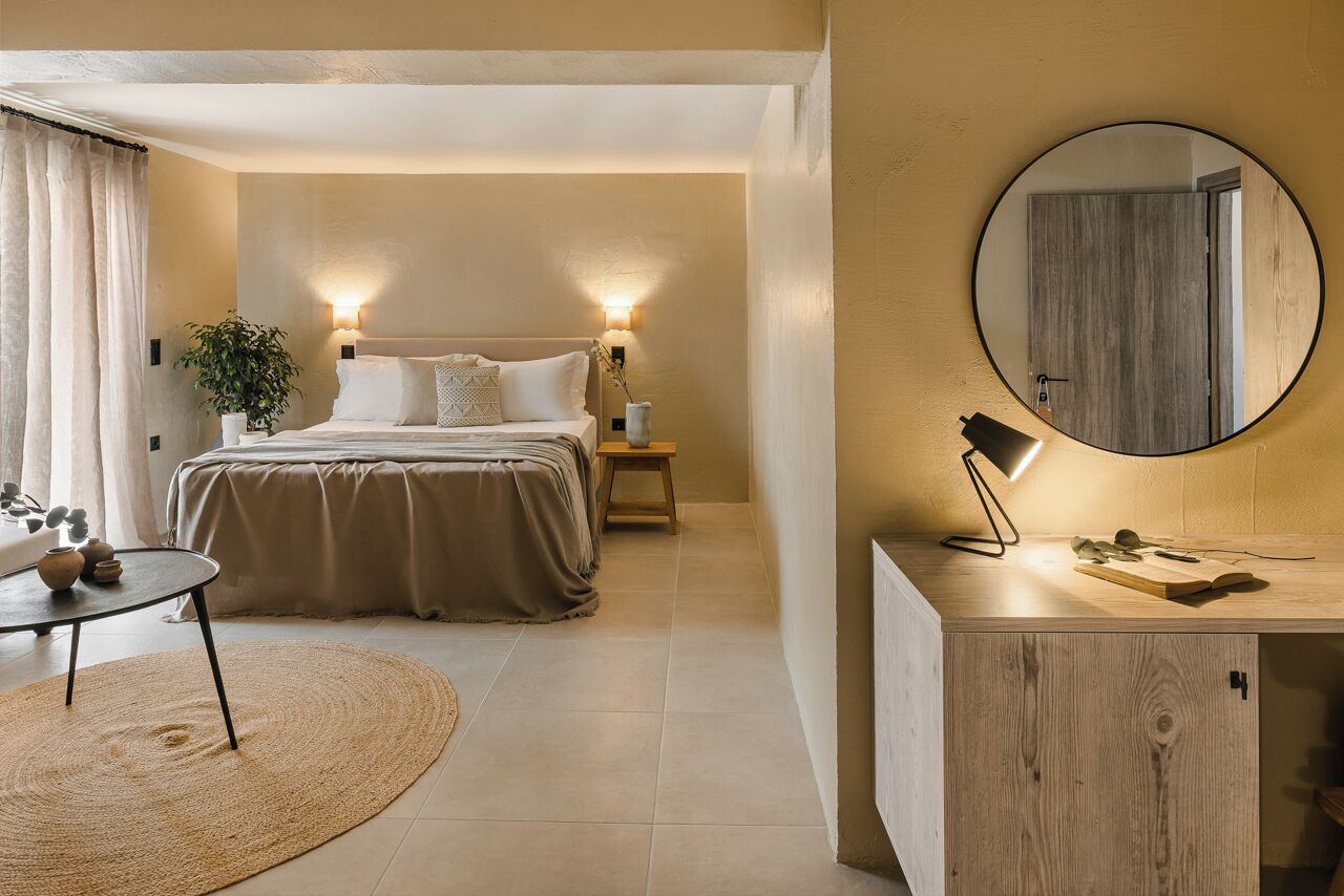 A modern bedroom with a large bed, bedside lamps, a round mirror, and a small table with a lamp.