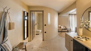 Un interior moderno con una pared curva, un banco de madera, un espejo, un bolso colgado y vistas a un baño.