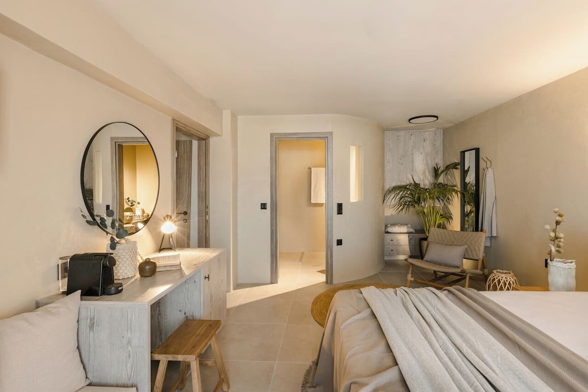 A modern hotel room with a bed, a desk, a chair, a mirror, and a plant.