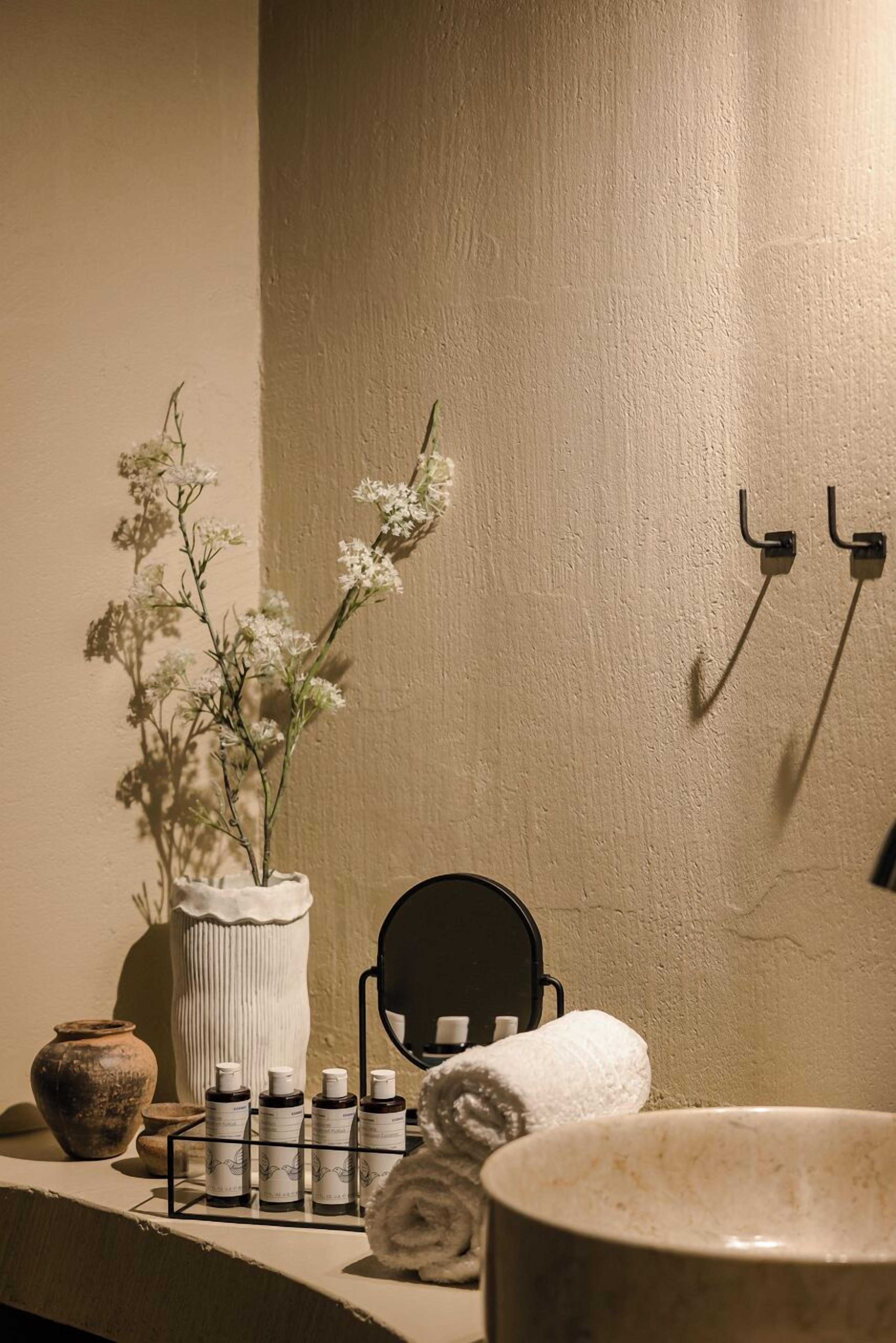 Een badkamer met een witte vaas met bloemen, een zwarte stoel, een handdoek en een plank met flessen.