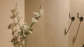 Een badkamer met een witte vaas met bloemen, een zwarte stoel, een handdoek en een plank met flessen.