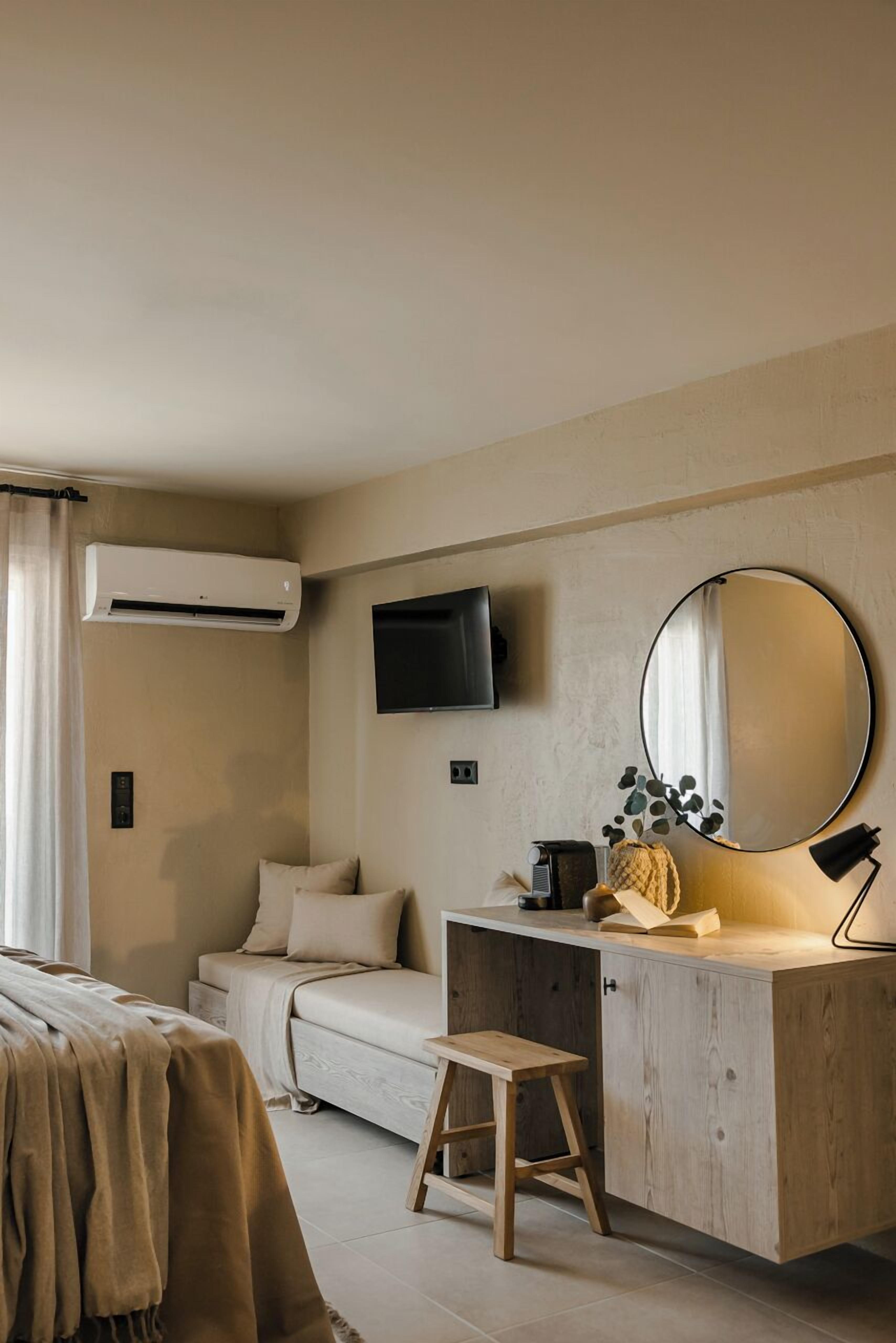 A bedroom with a bed, a desk, a chair, a TV, a mirror, and an air conditioning unit.