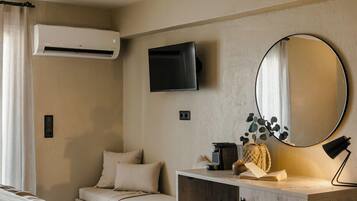 A bedroom with a bed, a desk, a chair, a TV, a mirror, and an air conditioning unit.