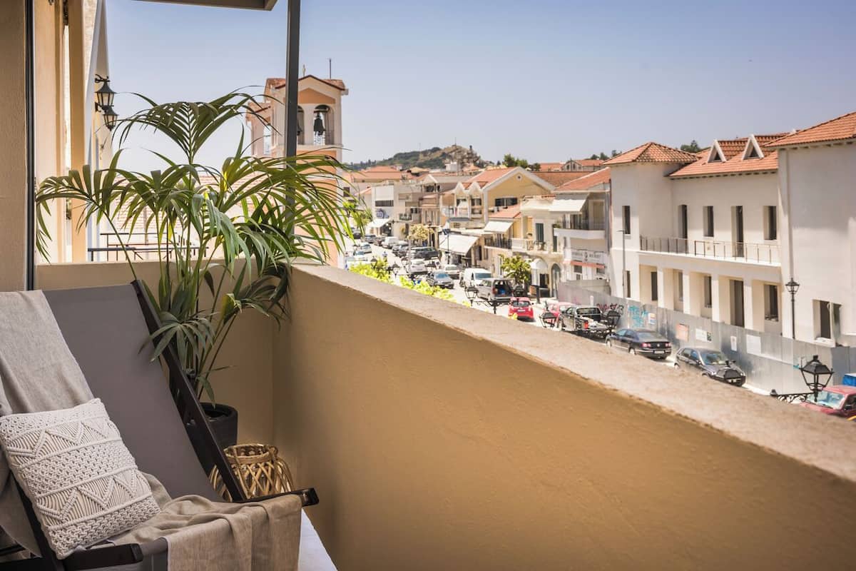 A balcony with a view of a street, a plant, and a chair with a cushion.