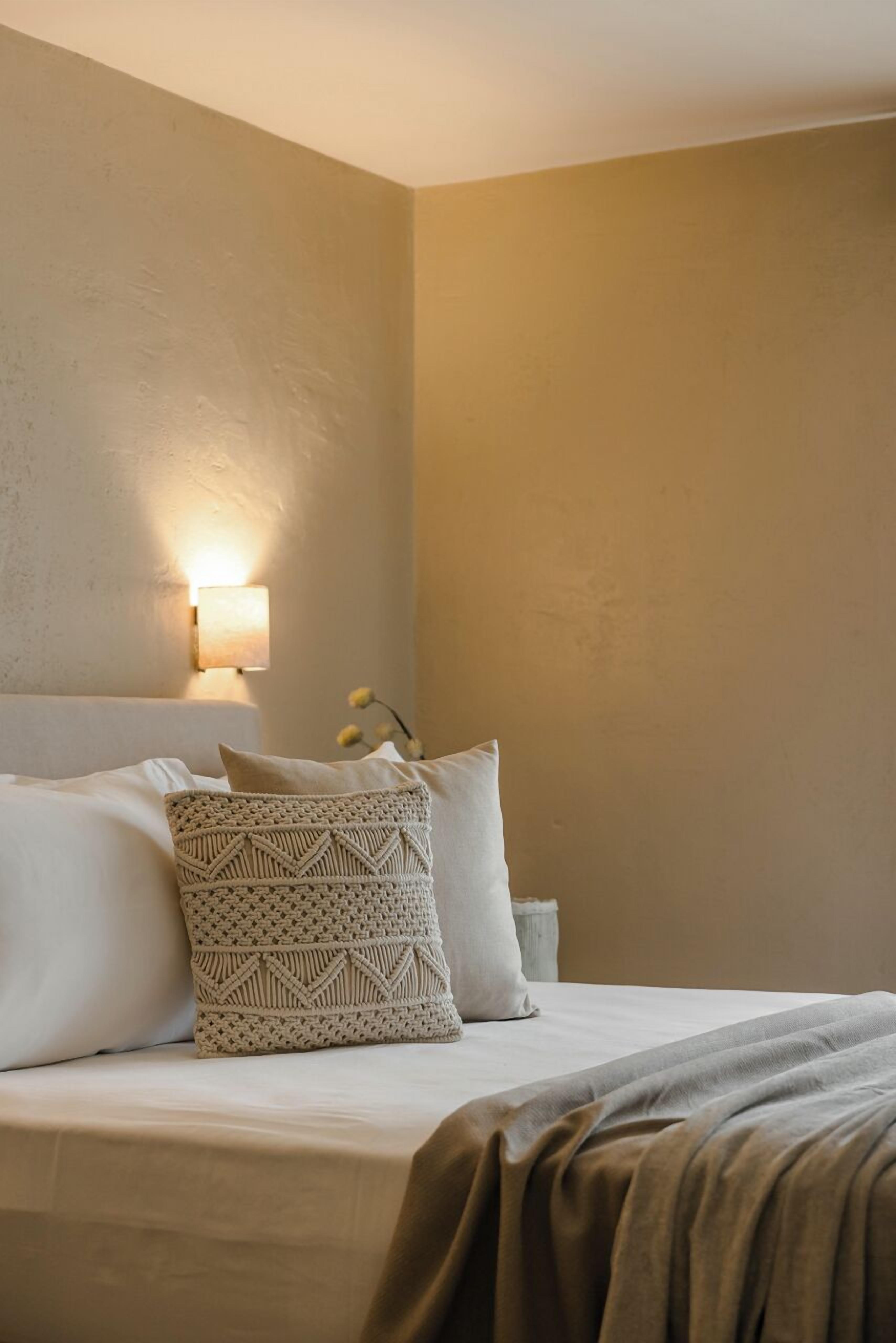 Ein Hotelzimmer mit einem Bett, einer Wandleuchte und einem kleinen Nachttisch mit Blumen in einer Vase.
