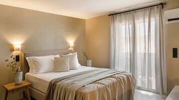Un dormitorio con cama, lámparas de noche, mesita de noche, ventana con cortinas translúcidas y aire acondicionado de pared.