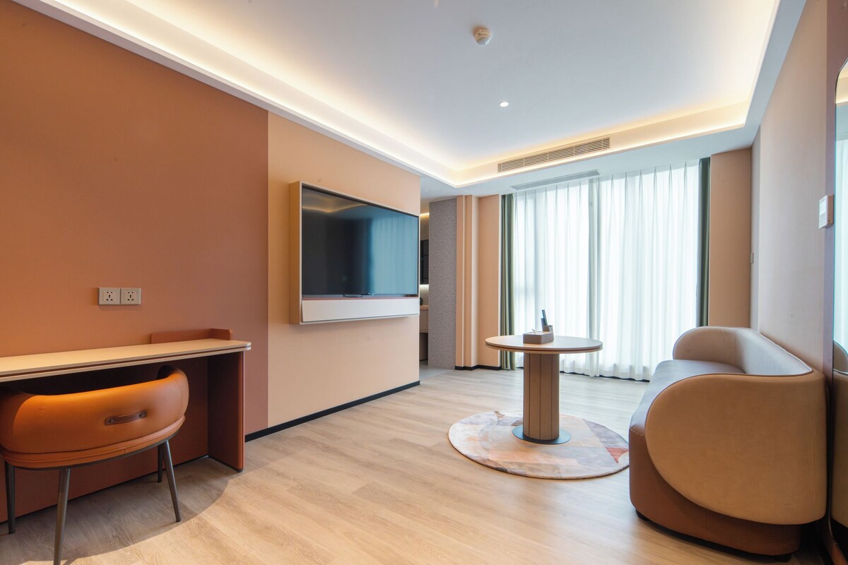 A modern hotel room with a flat-screen TV, a desk, a sofa, and a round table.