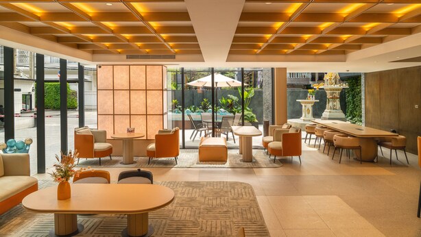 Eine moderne Hotelhalle mit einer zentralen Sitzgruppe, einem Empfangsbereich und Blick ins Freie.