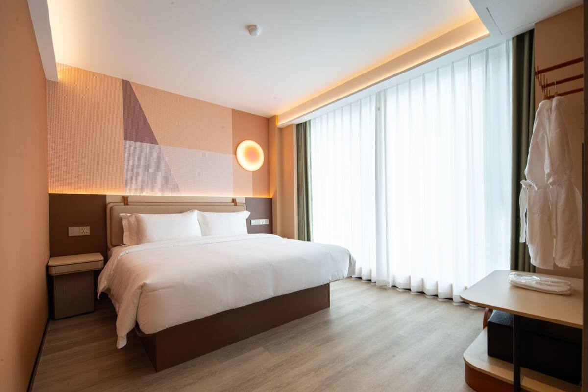 Ein Hotelzimmer mit Bett, Nachttisch und einem fenster mit Vorhängen.