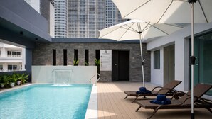 A rooftop pool with lounge chairs and umbrellas, a water feature, and a view of high-rise buildings. - Leston Hotel Sukhumvit (Bangkok)