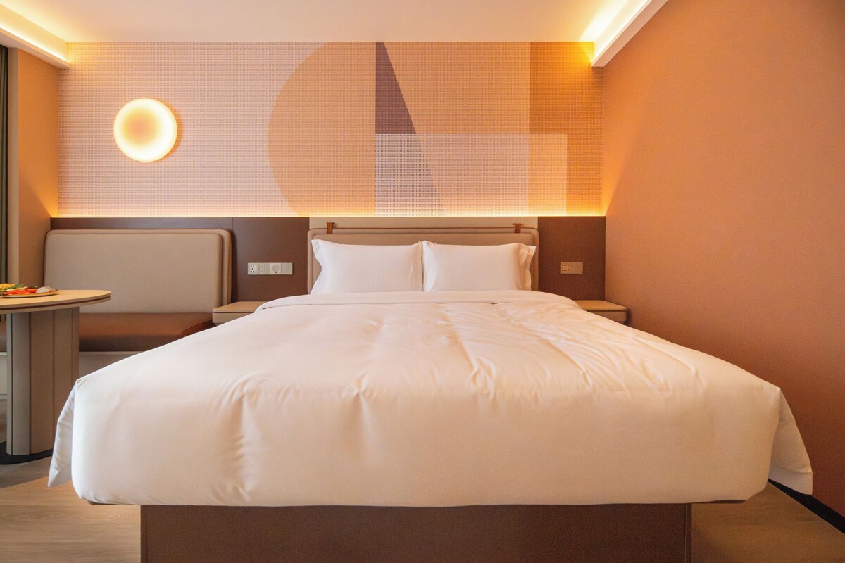 Een hotelkamer met een groot bed, nachtkastjes, een wandlamp en een klein tafeltje met een stoel.