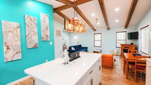 A modern kitchen with a white island, blue walls, wooden beams, and a dining area with a table and chairs. - Greek Spa • Private Acreage • Stonefire pizza oven (Front Royal)