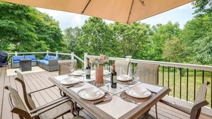 An outdoor dining area with a wooden deck, a table set for four, and a view of the surrounding greenery. - Greek Spa • Private Acreage • Stonefire pizza oven (Front Royal)