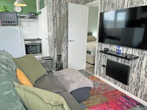 A modern living room with a sofa, TV, and kitchen area. - 2 bedroom accommodation in Bridlington (Bridlington)