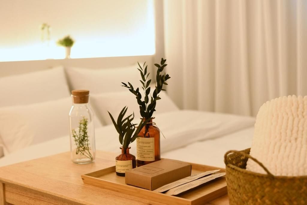 A wooden tray with a box, two small vases with plants, and a basket with a white towel on a bed.