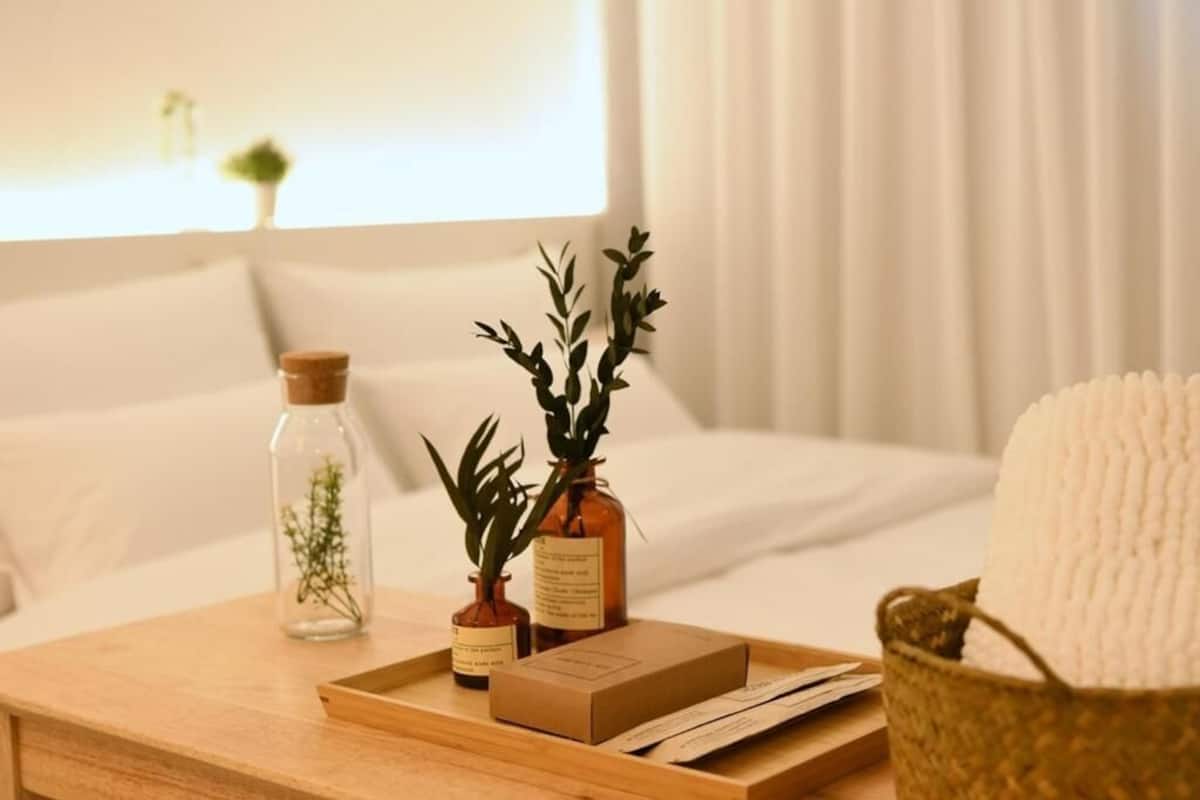 Un plateau en bois avec une boîte, deux petits vases contenant des plantes et un panier avec une serviette blanche sur un lit.