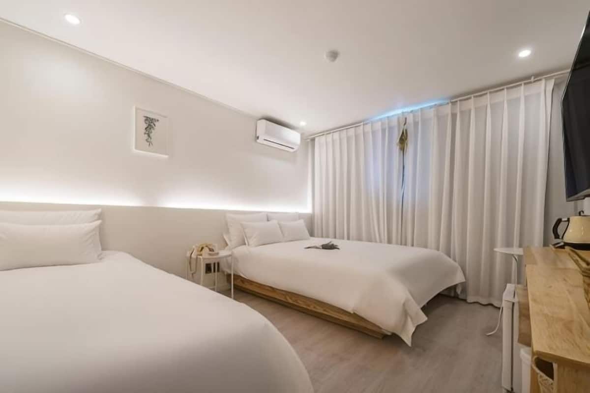 Une chambre d’hôtel avec deux lits, un bureau, une chaise, une télévision et une fenêtre avec des rideaux.