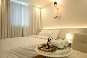 A hotel room with a neatly made bed, a bedside table with a lamp, and a wall-mounted light fixture. - hotelrawa (Seoul)