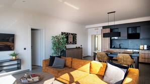 A modern living room with a sofa, a coffee table, and a dining area with chairs and a table. - Adriatic View Apartment by DuHomes (Dubrovnik)