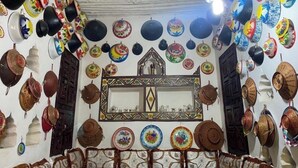A room with a variety of decorative plates and bowls hanging on the walls, a mirror with a decorative frame, and a patterned carpet on the floor. - Traditional Guest House  (Harar)