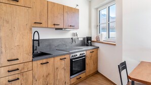Une cuisine compacte avec des meubles en bois, un évier noir, une cuisinière et une fenêtre donnant sur un immeuble.