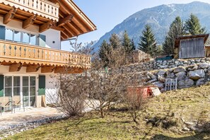 A traditional chalet with a balcony, stone walls, and a mountainous backdrop. - Apartment 'Beim Klarwein' with Mountain View, Shared Garden and Wi-Fi (Farchant)
