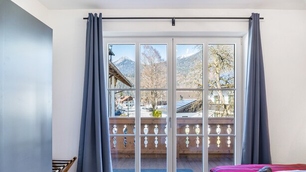 Une pièce dotée d’une grande porte-fenêtre coulissante donnant sur un balcon avec vue sur les montagnes et une terrasse en bois.