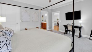 Un dormitorio con una cama grande, un escritorio, una silla, un televisor y un ventilador de techo.