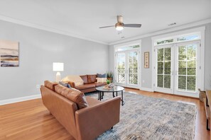 A living room with a brown leather sofa, a coffee table, a lamp, and a ceiling fan. - 5 Units w/ Free Parking • Walkable Historic District | The Juliette by AvantStay (Savannah)