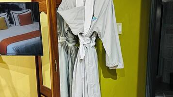 A bathroom with a wooden cabinet, a white robe hanging on the wall, and a bed with a red blanket.